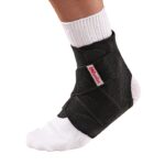 מגן קרסול לתמיכה - Adjustable Ankle Stabilizer של Mueller שחור רצועות מצטלבות על רגל שמאל עם גרב לבנה רצועות סגורות